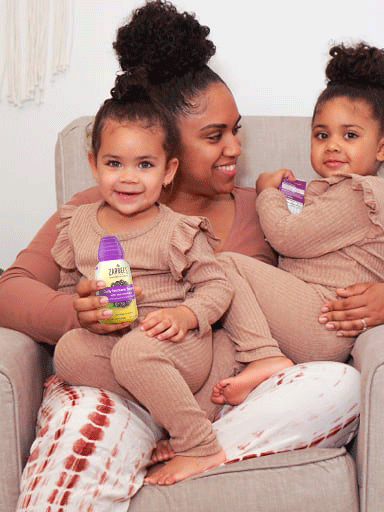 Mother sitting and smiling with two children while holding Zarbee's® product in right hand