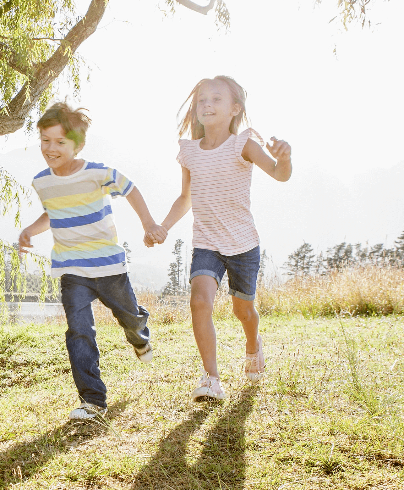 A boy and girl running and playing together with the sun shining behind them